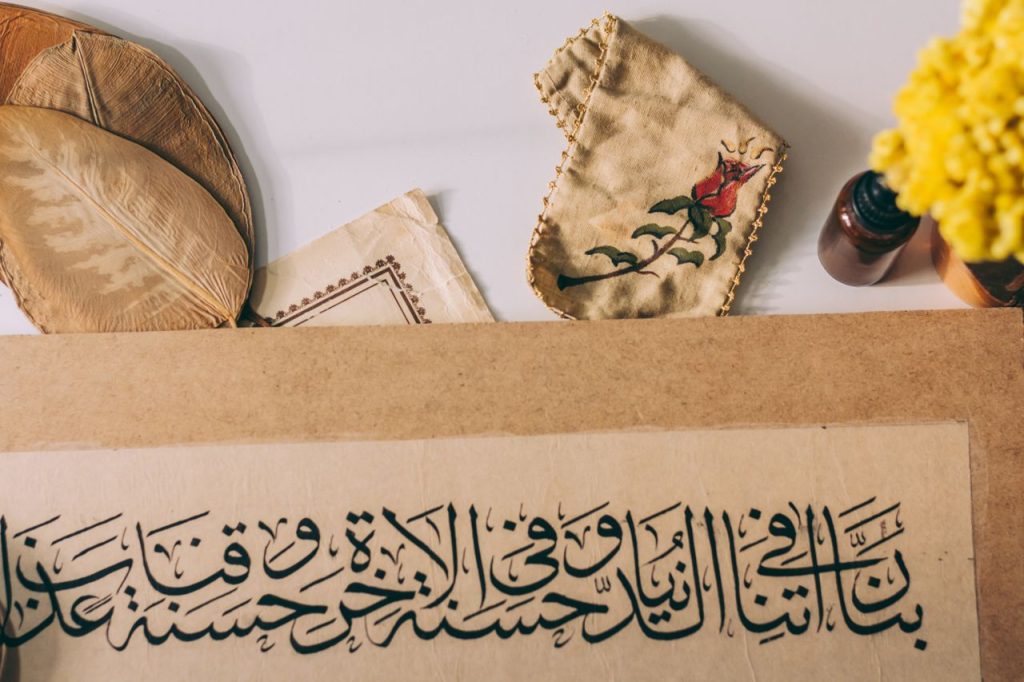 Arabic calligraphy art with a rose design, dried leaves, and a vibrant yellow flower on a desk.