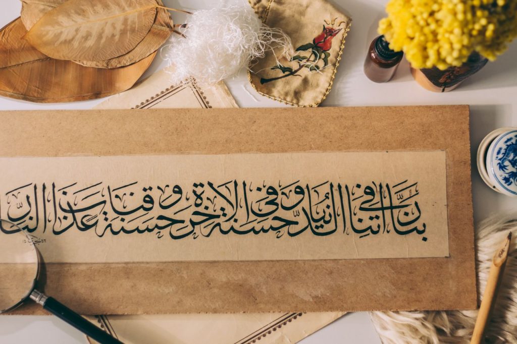 Elegant Arabic calligraphy surrounded by traditional art materials and flowers.